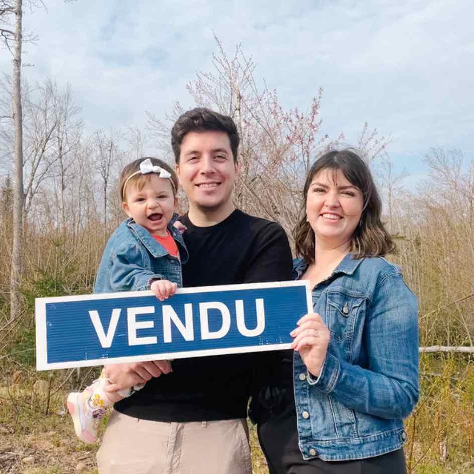 A family holding a sold sign in front of a vacant lot in Irishtown, New Brunswick